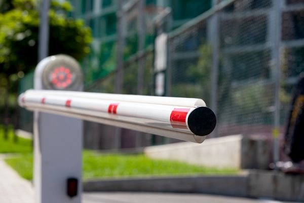 A white and red striped boom barrier at a gate, with a blurred background of a building