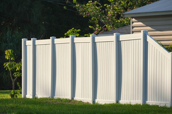 White vinyl privacy fence installed in a grassy yard, next to a house