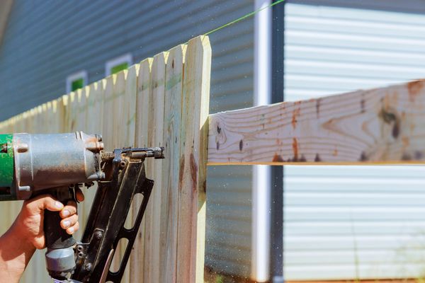 Close-up of a person using a nail gun to construct a wooden fence