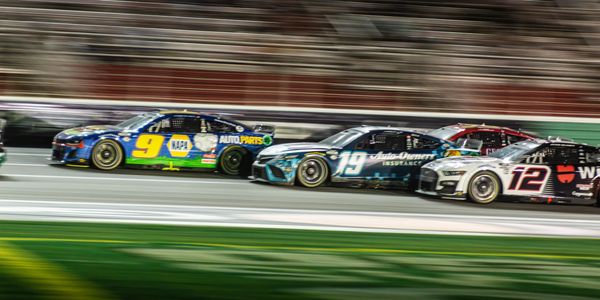 Three NASCAR cars racing closely on a track at night.