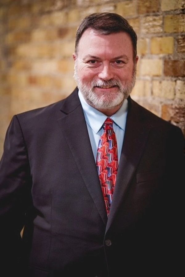Man in a suit with a patterned red tie smiling at the camera.