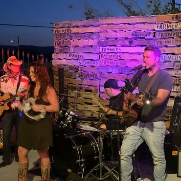 A lively outdoor country band performing at night with wooden pallets backdrop.