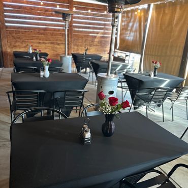 Cozy outdoor dining area with black tables, red rose centerpieces, and string lights.