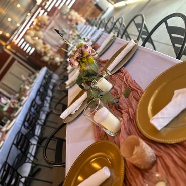 Elegant table setting with gold plates, white napkins, and floral centerpiece for an event.