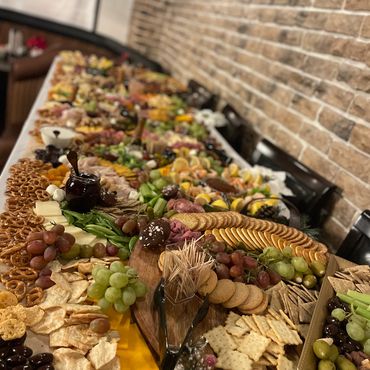 A large table filled with an assortment of crackers, cheeses, grapes, and dips.