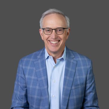 Smiling elderly man in glasses and blue checkered blazer.