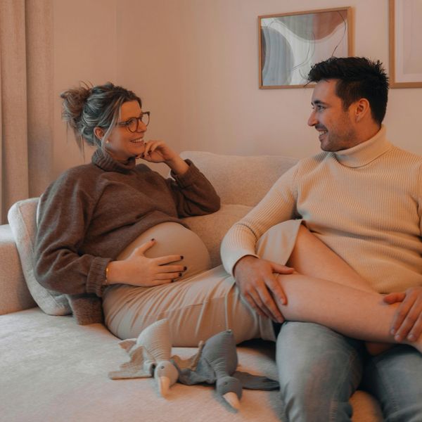 A pregnant woman and a man sit comfortably on a couch with a couple baby toys