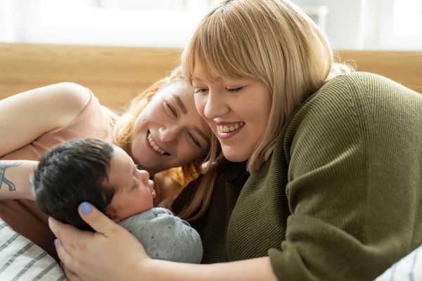 A lesbian couple is laying in bed admiring their newborn baby