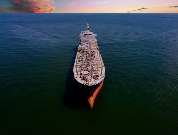 Large cargo ship sailing on calm ocean during sunset.