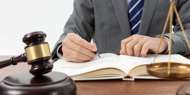 Person writing in a law book with gavel and scales nearby.