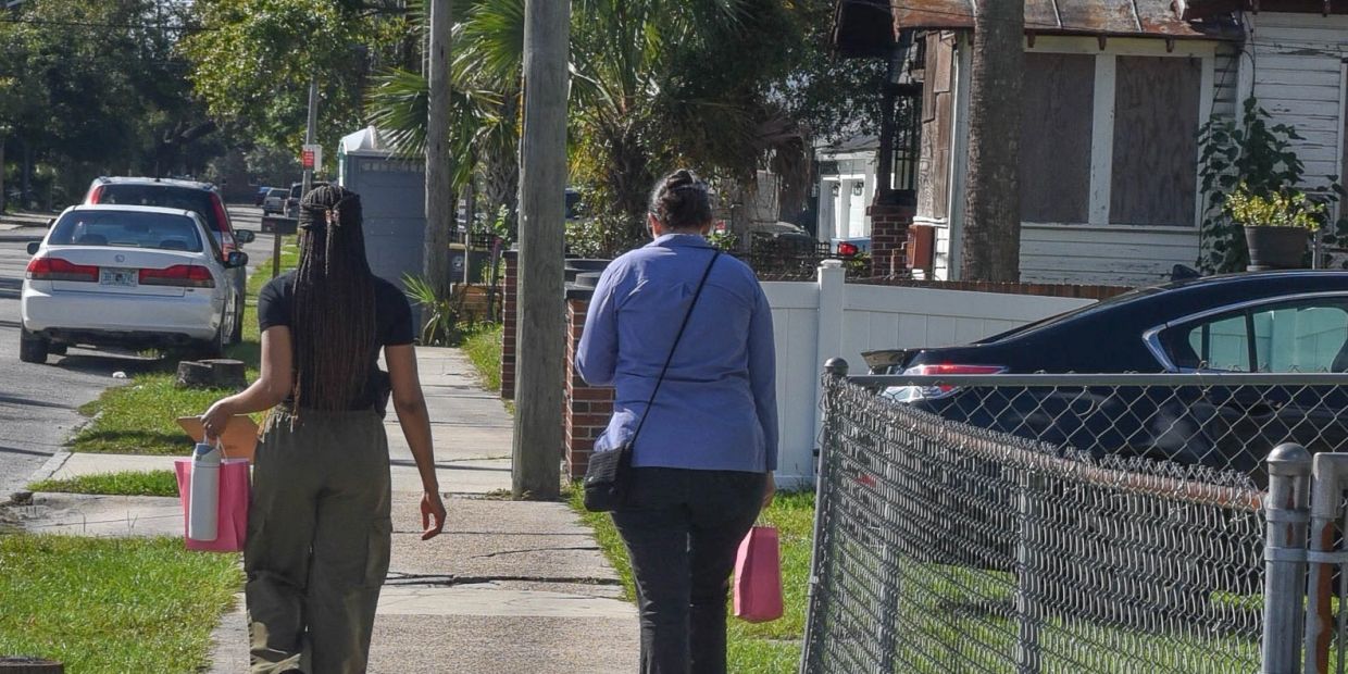Two women walking down a sidewalk carrying bags.