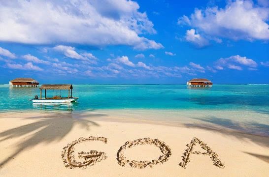 Beach scene in Goa with huts, boat, and clear blue waters.