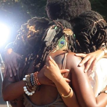 Three people with dreadlocks embrace warmly in a close group hug.