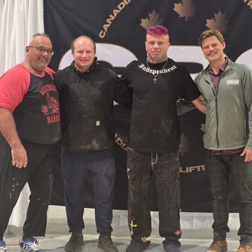 Four men standing together smiling in front of a Canadian flag backdrop.