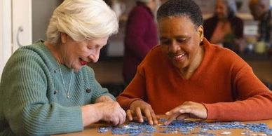 Two elderly women happily assembling a jigsaw puzzle together.