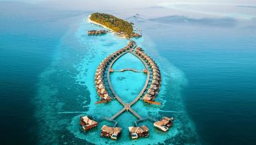 Aerial view of a tropical island resort with overwater bungalows.