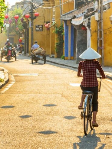 Person cycling on a sunny street lined with yellow buildings.