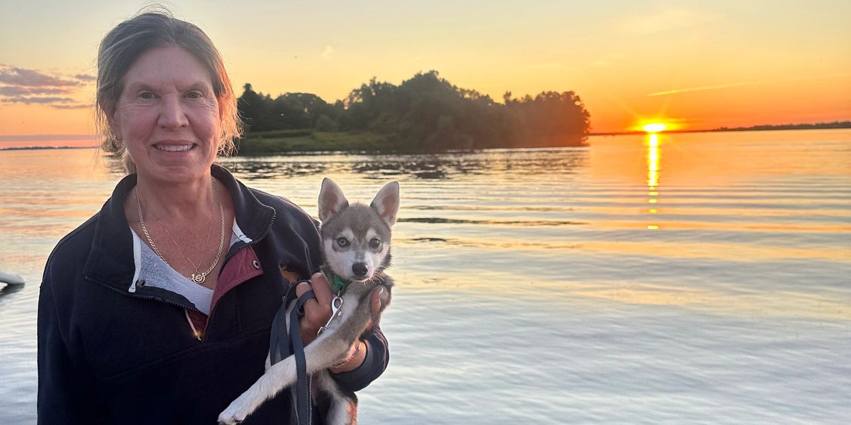 Woman holding a small dog at sunset by the water.