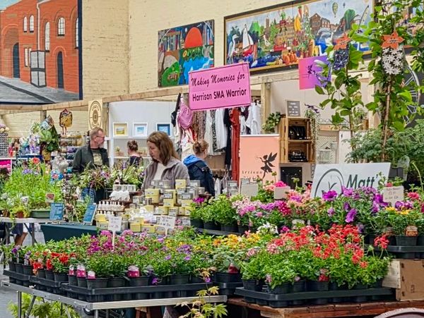 Indoor market with colorful flowers and handmade goods for a charity event.