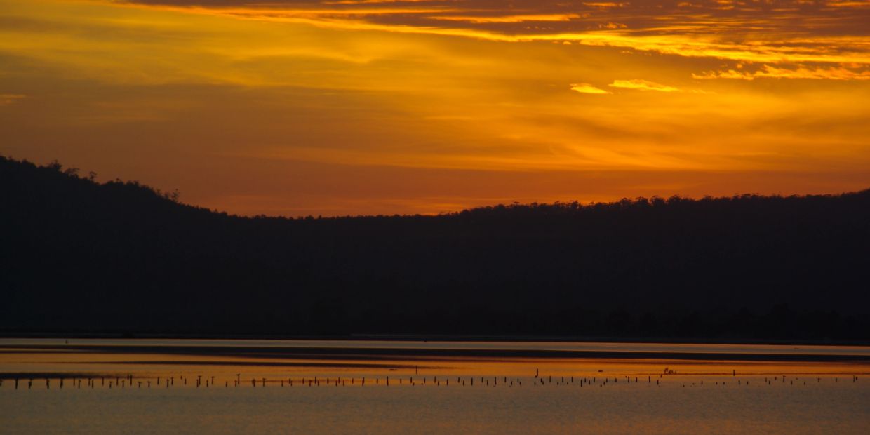 A serene sunset over a calm lake with silhouetted hills.