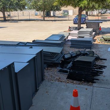 Stacks of metal panels and parts organized outdoors near parking area.