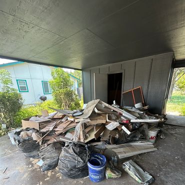 Pile of construction debris and garbage bags in a covered outdoor area.