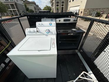 Washer, dryer, and oven placed together on a trailer outside.