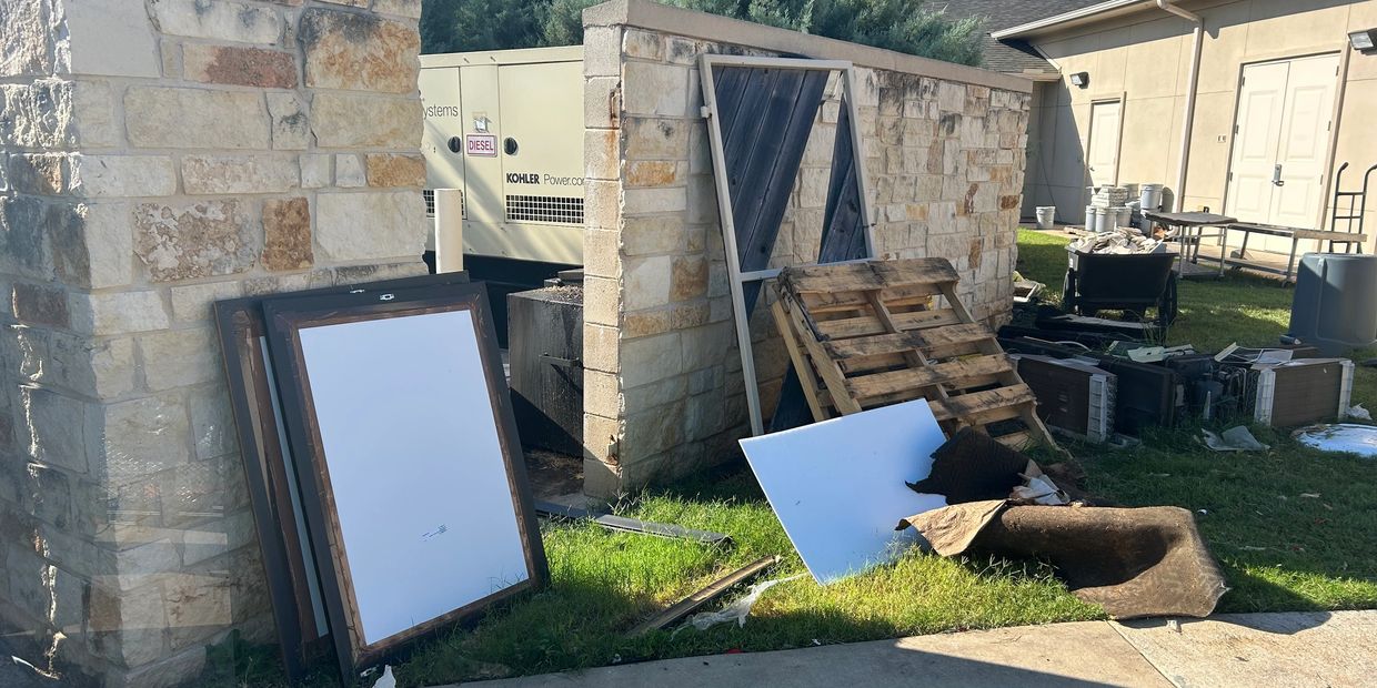 Discarded items and debris near a stone wall and building.