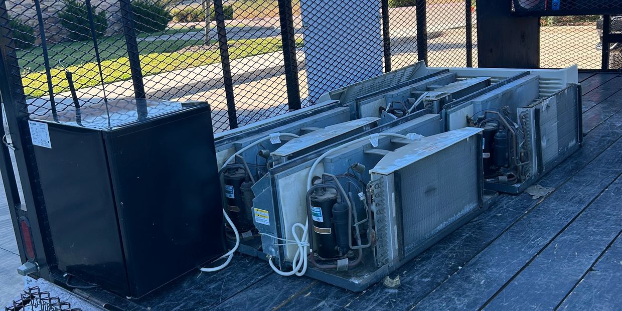 Damaged air conditioning units and a black refrigerator on a flatbed truck.