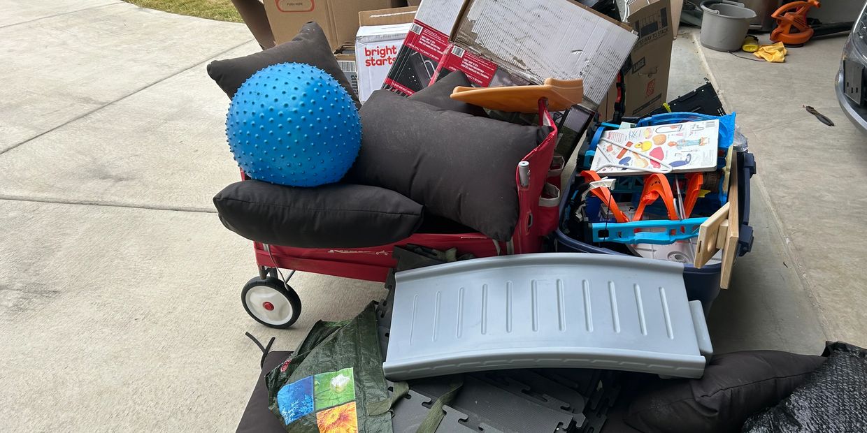 Outdoor pile of children's toys and cushions on a driveway.