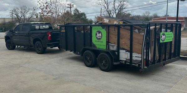 Black truck towing a trailer loaded with junk and advertising junk removal service.