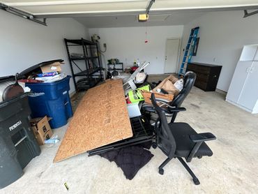 Cluttered garage with miscellaneous items and furniture scattered around.