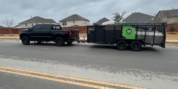 Black truck towing a trailer with junk removal items in a suburban neighborhood.
