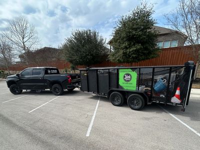 Black truck towing a large trailer with a junk removal sign in a parking lot.
