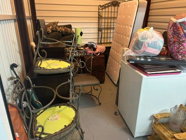 Storage unit filled with furniture, mattress, and bags.
