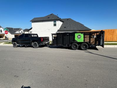 Black truck towing a trailer full of junk in a suburban neighborhood.