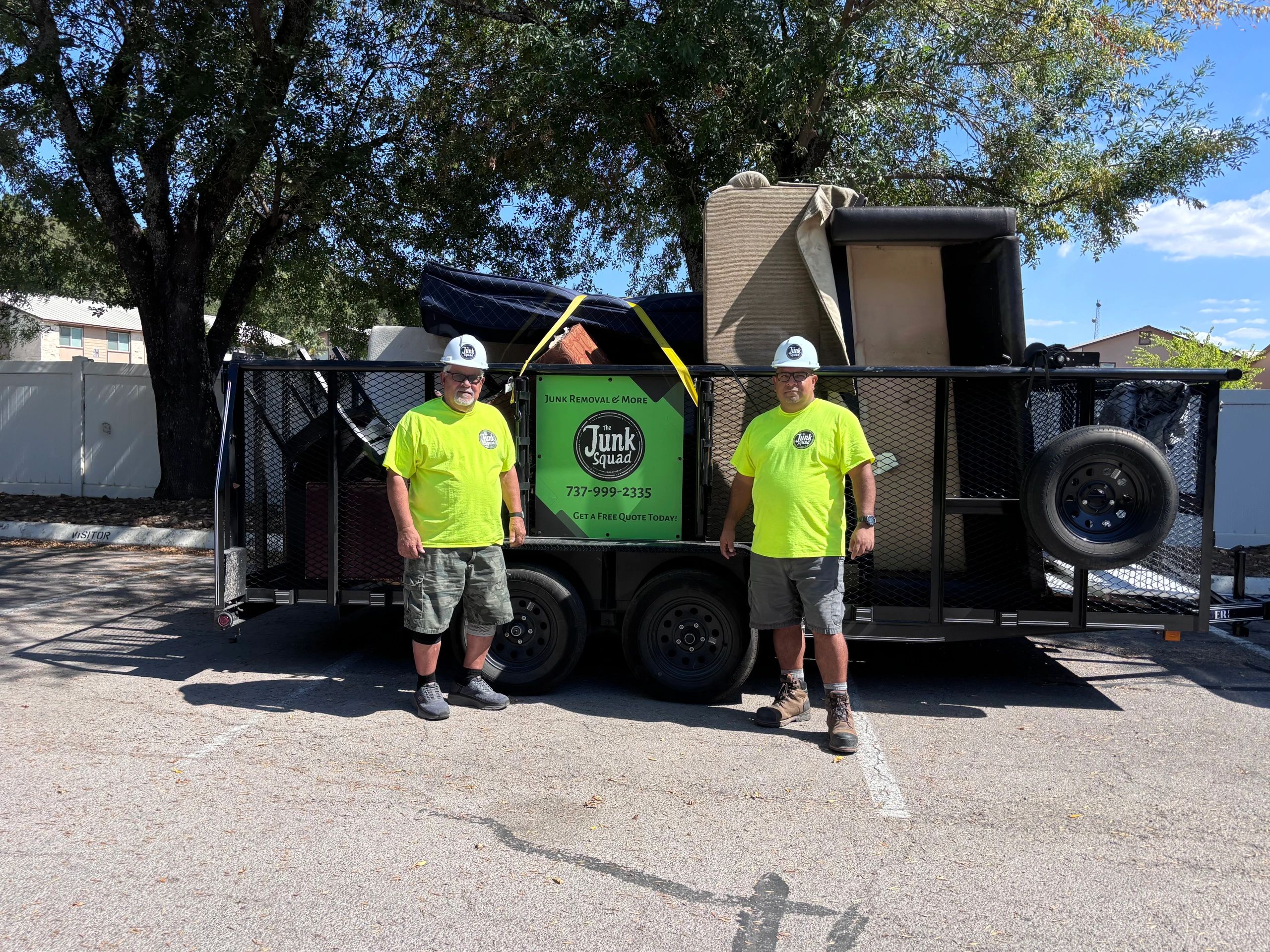 Two workers stand beside a trailer loaded with furniture for junk removal services.