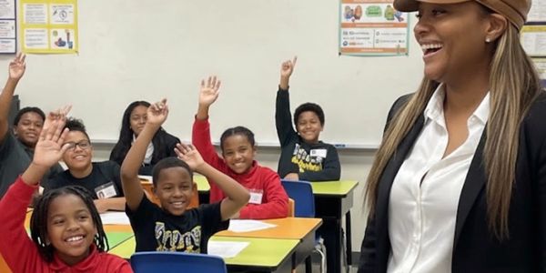 Happy students raising hands in a lively classroom with an enthusiastic teacher.