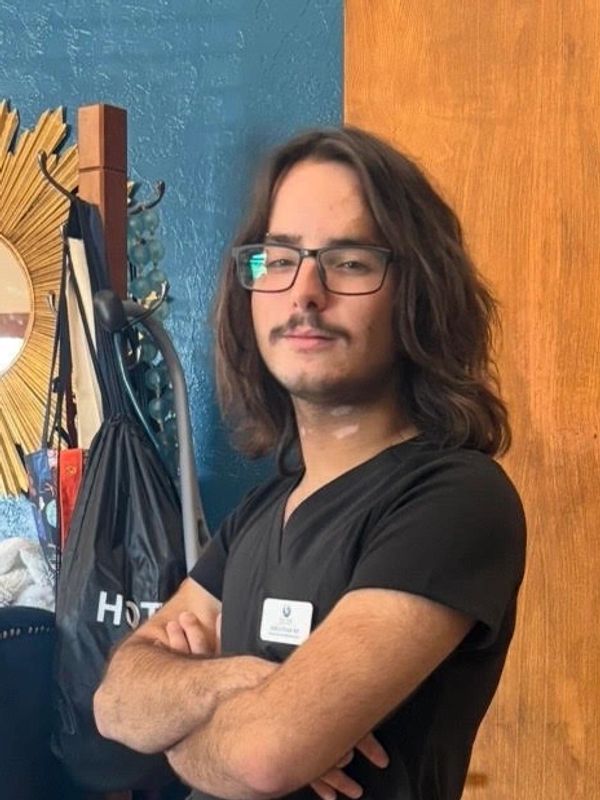 Man with long hair and glasses standing confidently with folded arms.