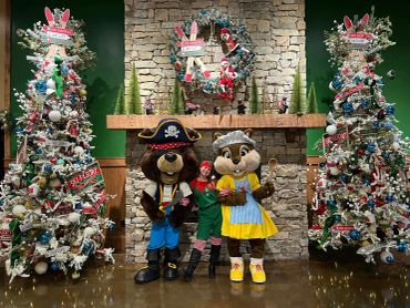 Two animal mascots and a person in a festive elf costume pose happily indoors.