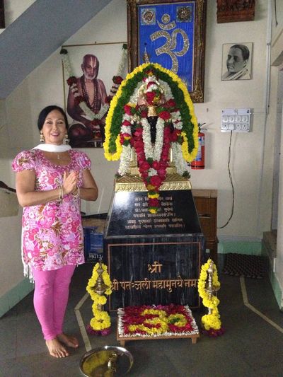 Woman in traditional attire praying beside a decorated Hindu shrine indoors.