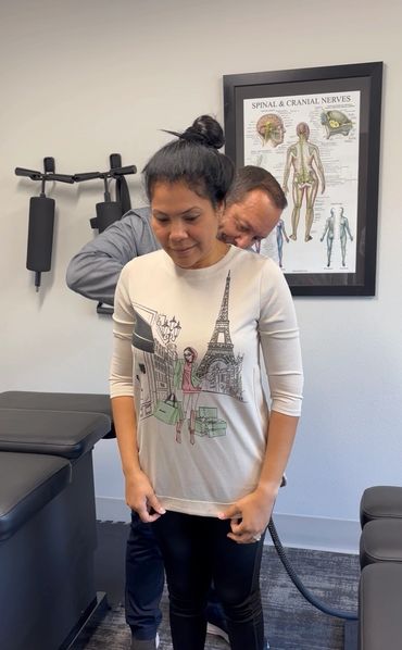 A chiropractor adjusts a woman's back in a clinic with spinal anatomy poster.