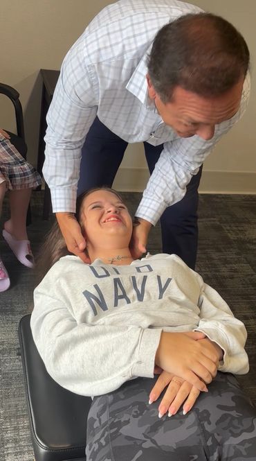 A man adjusts a smiling woman's neck while she lies on a table.