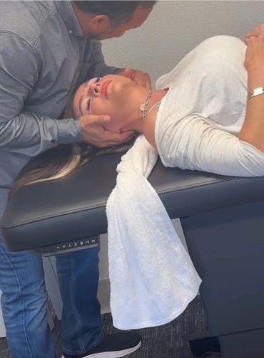 A chiropractor adjusts a woman's neck as she lies on a treatment table.