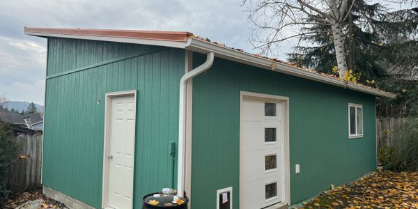 Small green shed with two doors and a slanted roof in autumn setting.