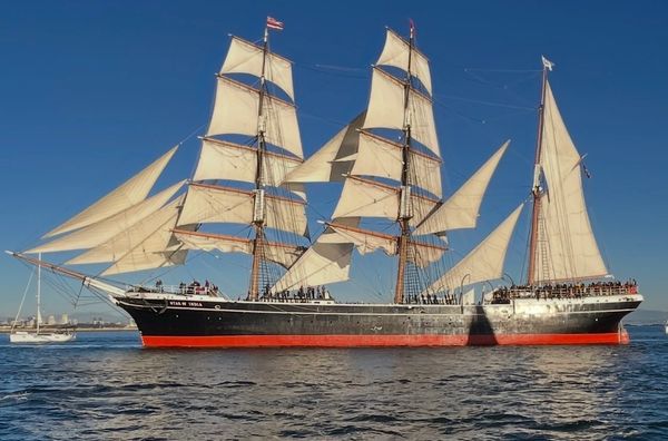 Tall ship with full sails on water under clear sky.