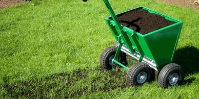 A seed spreader filled with soil on grass.