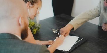 Two people signing a document while a third person points.