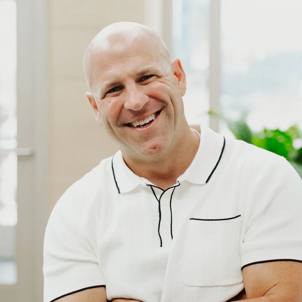 Man in a white shirt standing indoors with arms crossed, smiling.