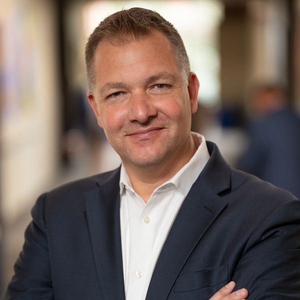 Man in a blue jacket smiling against a hotel lobby backdrop.